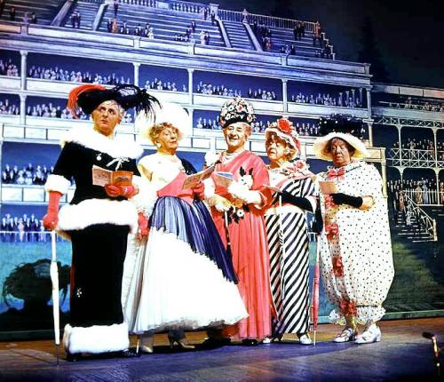 This photograph shows The Crazy Gang in their 1959 show Clown Jewels. It is a skit on the famous black and white Ascot scene designed by Cecil Beaton for the musical My Fair Lady which was the current box office hit in London. 